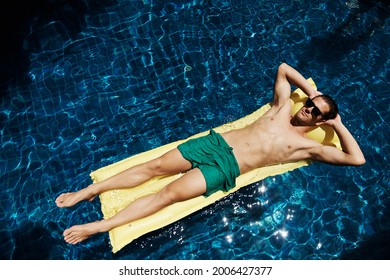 Shot of a relaxed young man floating on a lilo in a blue pool - Powered by Shutterstock