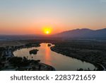 a shot of the rippling waters of the Santa Fe Reservoir with a stunning orange sunset with lush green trees and majestic mountain ranges at Santa Fe Dam Recreation Area in Irwindale California