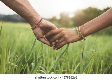 Shot Of Romantic Couple Holding Hands In A Field. Close Up Shot Of Man And Woman With Hand In Hand Walking Through Grass Field.