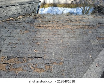 A shot of a rooftop with lots of missing shingles. The roof is severely damaged, weathered, decaying, rotting, and in need of repair or replacement.