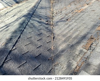 A shot of a rooftop with lots of missing shingles. The roof is severely damaged, weathered, decaying, rotting, and in need of repair or replacement.