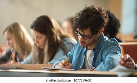 Shot of a Row of Multi Ethnic Students in the Classroom Taking Exam/ Test. Focus on Holding Pens and Writing in Notebooks. Bright Young People Study at University. - Shutterstock ID 1077839606
