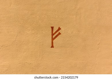 shot of a runic letter drawn on a yellow wall, the specific rune is Fehu