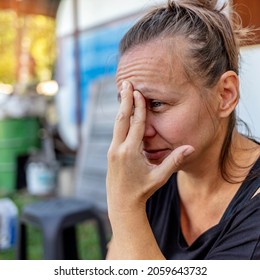 Shot Of Sad Woman Sitting Outdoor. Woman Outdoors In Nature Holding Her Head Expressing Pain, Exhaustion, Sadness Or Depression. Concerned Serious Mature Woman. Photo Of A Beautiful Thoughtful Female.