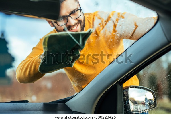 Shot of a satisfied man cleaning the windows on\
his car from outside.