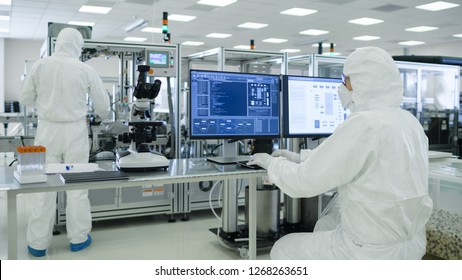 Shot of a Scientists in Sterile Suits Working with Computers, Analyzing Data form Modern Industrial Machinery in the Laboratory. Product Manufacturing Process: Pharmaceutics, Semiconductors
