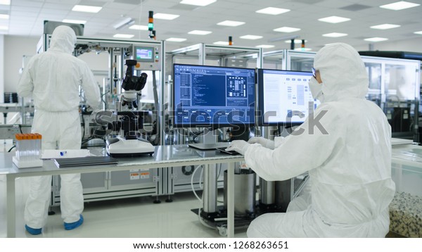 Shot\
of a Scientists in Sterile Suits Working with Computers, Analyzing\
Data form Modern Industrial Machinery in the Laboratory. Product\
Manufacturing Process: Pharmaceutics,\
Semiconductors