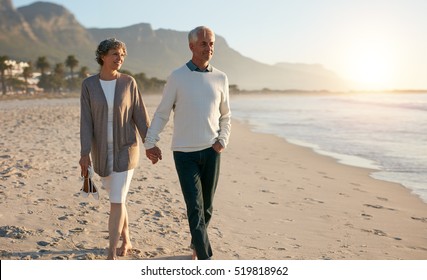 Shot of senior couple walking along beach together holding hands. - Powered by Shutterstock