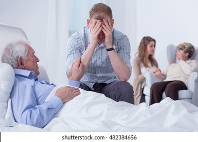 Shot Of A Senior Man Laying On A Hospital Bed And His Son Sitting Next To Him And Crying