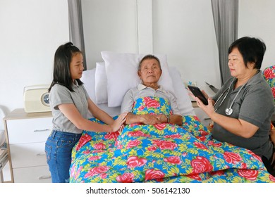 Shot Of A Senior Man Laying On A Hospital Bed And Answering To His Doctor's Questions With Tablet, Family Member Around Grandfather Bed. Doctor Using Digital Tablet Talking With Senior Patient