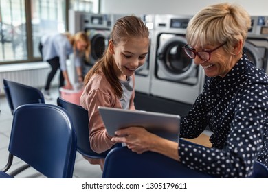 Shot Of A Senior Woman And Her Granddaughter Using Technology While Waiting Laundry Done At Laundromat