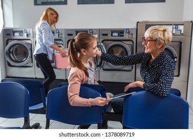 Shot Of A Senior Woman And Her Granddaughter Using Technology While Waiting Laundry Done At Laundromat