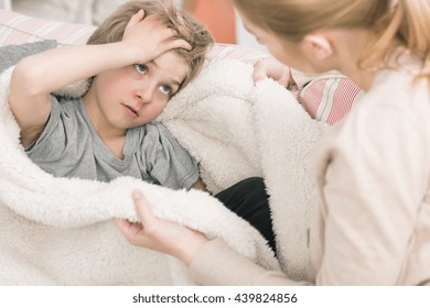 Shot Of A Sick Little Boy Holding His Head And Talking To His Mum