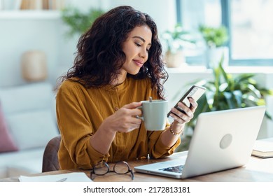 Shot of smart business woman using mobile phone while drinking a cup of coffee in living room at home. - Powered by Shutterstock