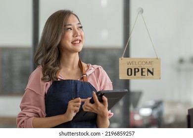 Shot Of Smiling Asian Young Sme Small Business Owner Wearing Apron And Standing White Ipad And Open Sign Coffee Shop Door, Asian Business Woman Barista Cafe Owner SME Entrepreneur Seller Concept