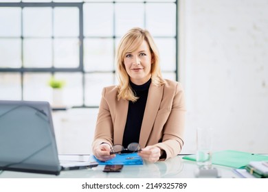 Shot Of Smiling Blond Businesswoman Sitting At Desk Behind Her Laptop And Working. Home Office.