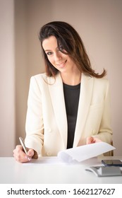 Aufnahme einer lächelnden Geschäftsfrau, die am Schreibtisch sitzt und den Vertrag während der Arbeit unterzeichnet. 