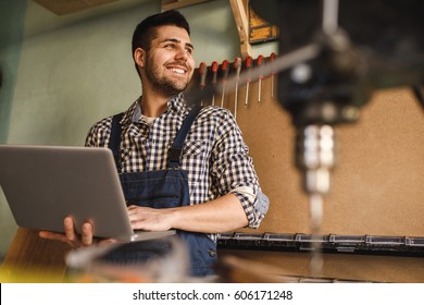 Shot of a smiling carpenter using laptop at work in workshop. - Powered by Shutterstock