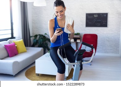 Shot of smiling fitness girl using mobile phone after training on exercise bike at home. - Powered by Shutterstock