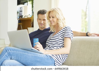 Shot Of A Smiling Middle Aged Couple Sitting On Couch And Using Credit Card And Laptop While Shopping Online. 