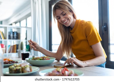 Shot of smiling woman eating healthy food while using her mobile phone at home. - Powered by Shutterstock