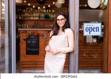 Shot of smiling young cafe show owner woman standing with arms crossed in the doorway. Open sign on the glass door. - Shutterstock ID 1891392661