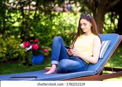 Shot of smiling young woman using her mobile phone and text messaging while relaxing in the garden at home. 