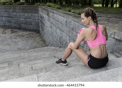 Shot of a sportswoman with braided hair, sitting on the steps and holding a water bottle - Powered by Shutterstock