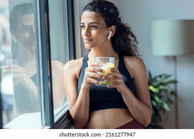 Shot of sporty woman drinking detox water while taking a break of doing exercise in living room at home.