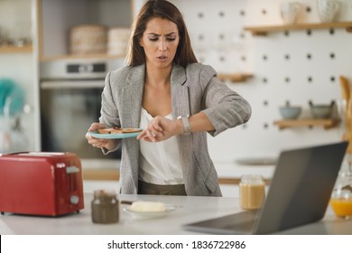Shot of a stressed multi-tasking young business woman having a breakfast and using laptop in her kitchen while getting ready to go to work. - Shutterstock ID 1836722986