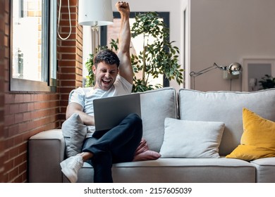 Shot of successful young man using her laptop and celebrating something while sitting on sofa at home.
