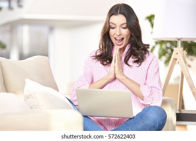 Shot of a surprised young woman using her laptop while sitting on couch at home.  - Shutterstock ID 572622403