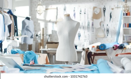 Shot of a Tailoring Mannequin that Stands in a Bright and Sunny Studio. Various Sewing Items and Colorful Fabrics Laying around, Mannequins Standing, and Sketches Pinned to the Wall. - Powered by Shutterstock