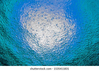 A Shot Taken From Beneath The Surface Of The Sea Looking Up At The Sky. The Light Patch Is The Sun Overhead And Through The Surface It Is Possible To See The Rain Falling Hard On The Water