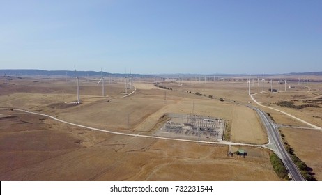 Shot taken with drone of spacious desert with plenty of windmills producing energy and plantation with roadways in bright sunlight.