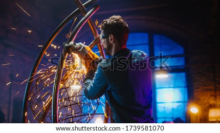 Shot of Talented Innovative Artist Using an Angle Grinder to Make an Abstract, Brutal and Expressive Metal Sculpture in a Workshop. Contemporary Fabricator Creating Modern Steel Art.