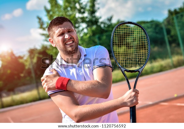 Shot of a tennis player with a shoulder injury on a\
clay court