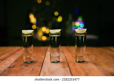 Shot Of Tequila Served In A Tequila Glass On A Wooden Table. Blurred Background. Rustic Bar Atmosphere.