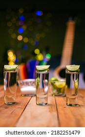 Shot Of Tequila Served In A Tequila Glass On A Wooden Table. Blurred Background. Rustic Bar Atmosphere.