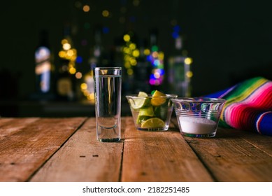 Shot of tequila served in a tequila glass on a wooden table. Blurred background. Rustic bar atmosphere.