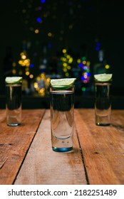 Shot Of Tequila Served In A Tequila Glass On A Wooden Table. Blurred Background. Rustic Bar Atmosphere.