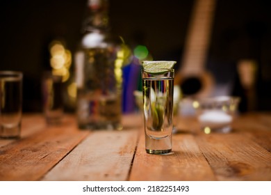 Shot Of Tequila Served In A Tequila Glass On A Wooden Table. Blurred Background. Rustic Bar Atmosphere.