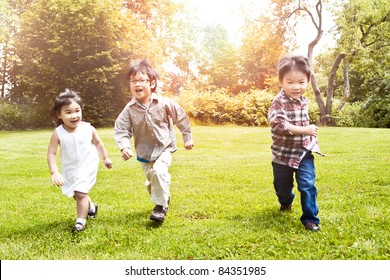 A Shot Of Three Asian Kids Running In A Park (focus In The Middle Kid)