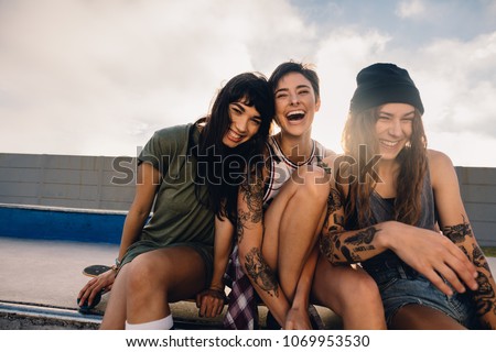 Shot of three smiling girls hanging out at skate park. Group of women friends sitting outdoors at skate park and laughing.
