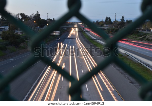 Shot through chain-linked fence toward highway\
with long exposure.