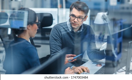 Shot Through Glass in Modern Factory: Female Project Supervisor Talks to a Male Industrial Engineer who Works on Personal Computer. Modern High-Tech Industrial Factory Office.