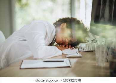 Shot Of A Tired African Female Doctor Laying Down On Her Crossed Arms At Desk While Looking X-ray On Computer During COVID-19 Pandemic.