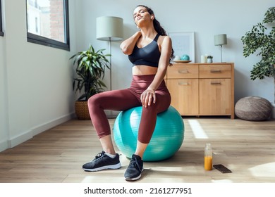 Shot of tired young sporty woman suffering neck pain while doing exercise with the ball at home.