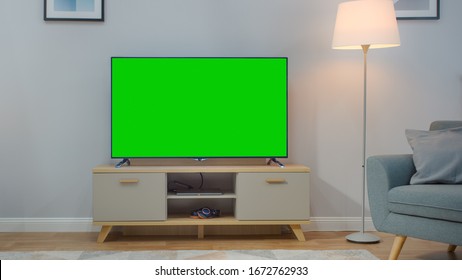 Shot Of A TV With Horizontal Green Screen Mock Up. Cozy Living Room At Day Time With A Chair And Lamps Turned On At Home.