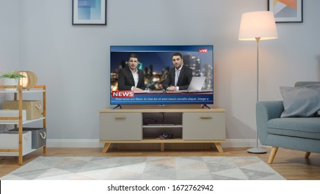 Shot Of A TV With Live News Channel. Cozy Living Room At Day Time With A Chair And Lamps Turned On At Home.